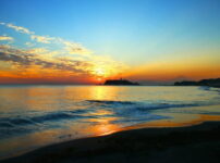 夕暮れの海に静かな波が寄せる中、遠くの小さな島と塔が淡く浮かぶ情景｜懐かしい情景が静かによみがえる、やさしい記憶のイメージ写真