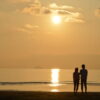 夕暮れの海辺で寄り添う2人の後ろ姿が静かに映る情景｜懐かしい情景が静かによみがえる、やさしい記憶のイメージ写真
