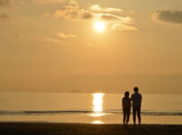 夕暮れの海辺で寄り添う2人の後ろ姿が静かに映る情景｜懐かしい情景が静かによみがえる、やさしい記憶のイメージ写真
