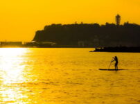夕暮れの海辺で静かにパドルボードを漕ぐ人のシルエット｜懐かしい情景が静かによみがえる、やさしい記憶のイメージ写真