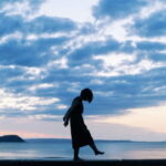 夕暮れの海辺に佇む人物のシルエット｜懐かしい情景が静かによみがえる、やさしい記憶のイメージ写真