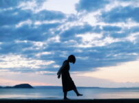 夕暮れの海辺に佇む人物のシルエット｜懐かしい情景が静かによみがえる、やさしい記憶のイメージ写真