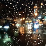 夜の雨粒がついた窓越しに、街の灯りが静かにぼけて滲む情景｜懐かしい情景が静かによみがえる、やさしい記憶のイメージ写真
