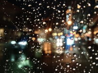 夜の雨粒がついた窓越しに、街の灯りが静かにぼけて滲む情景｜懐かしい情景が静かによみがえる、やさしい記憶のイメージ写真