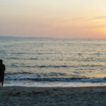 夕暮れの海辺で女性が静かに佇む情景｜懐かしい情景が静かによみがえる、やさしい記憶のイメージ写真