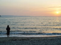 夕暮れの海辺で女性が静かに佇む情景｜懐かしい情景が静かによみがえる、やさしい記憶のイメージ写真