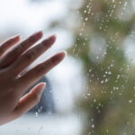 雨粒のついた窓ガラスにそっと触れる手の情景｜懐かしい情景が静かによみがえる、やさしい記憶のイメージ写真
