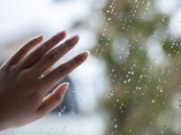 雨粒のついた窓ガラスにそっと触れる手の情景｜懐かしい情景が静かによみがえる、やさしい記憶のイメージ写真