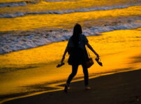 夕暮れの海辺を裸足で歩く女性のシルエット｜懐かしい情景が静かによみがえる、やさしい記憶のイメージ写真