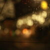 雨粒のついた窓越しに、夜の街の灯りがやわらかく滲む情景｜懐かしい情景が静かによみがえる、やさしい記憶のイメージ写真