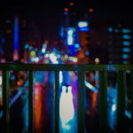 フェンス越しに滲むネオンの光が広がる、静かな都会の夜景|懐かしい情景が静かによみがえる、やさしい記憶のイメージ写真