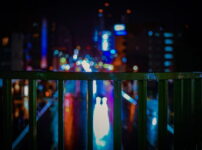フェンス越しに滲むネオンの光が広がる、静かな都会の夜景｜懐かしい情景が静かによみがえる、やさしい記憶のイメージ写真