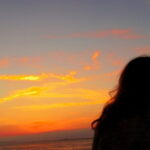夕暮れの海辺で女性が静かに佇む後ろ姿の情景|懐かしい情景が静かによみがえる、やさしい記憶のイメージ写真
