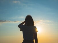 夕暮れの光に照らされながら静かに佇む女性のシルエット｜懐かしい情景が静かによみがえる、やさしい記憶のイメージ写真