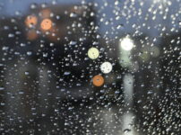 雨粒がついた窓越しに、ぼんやりと街の灯りがにじむ夜の情景｜懐かしい情景が静かによみがえる、やさしい記憶のイメージ写真