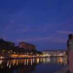 夕暮れの水辺で都会の灯りを静かに見つめる女性の後ろ姿|懐かしい情景が静かによみがえる、やさしい記憶のイメージ写真