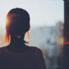 夕暮れの窓辺で夕日を見つめる女性の後ろ姿と柔らかな光｜懐かしい情景が静かによみがえる、やさしい記憶のイメージ写真