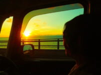 夕暮れの海を車内から静かに見つめる人物のシルエット｜懐かしい情景が静かによみがえる、やさしい記憶のイメージ写真