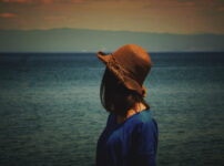 夕暮れの水辺を静かに見つめる女性の後ろ姿｜懐かしい情景が静かによみがえる、やさしい記憶のイメージ写真