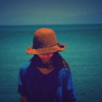 海辺で帽子をかぶった女性が静かに佇む姿の風景｜懐かしい情景が静かによみがえる、やさしい記憶のイメージ写真