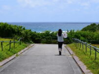 海へ続く小道をそっと歩く女性の後ろ姿｜懐かしい情景が静かによみがえる、やさしい記憶のイメージ写真