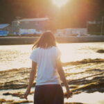 夕暮れの海辺で女性がそっと佇む後ろ姿の情景｜懐かしい情景が静かによみがえる、やさしい記憶のイメージ写真