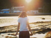 夕暮れの海辺で女性がそっと佇む後ろ姿の情景｜懐かしい情景が静かによみがえる、やさしい記憶のイメージ写真