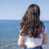 海辺で女性が静かに海を見つめる後ろ姿の情景｜懐かしい情景が静かによみがえる、やさしい記憶のイメージ写真