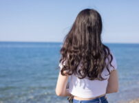 海辺で女性が静かに海を見つめる後ろ姿の情景｜懐かしい情景が静かによみがえる、やさしい記憶のイメージ写真