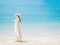 夏の海辺で、ワンピース姿の女性が静かに海を見つめる後ろ姿の情景｜懐かしい情景が静かによみがえる、やさしい記憶のイメージ写真