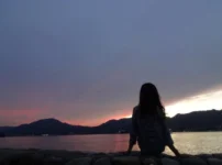 夕暮れの海辺で、静かに座る人物の後ろ姿が映る情景｜懐かしい情景が静かによみがえる、やさしい記憶のイメージ写真