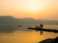 夕暮れの湖畔に柔らかな光が広がり、桟橋に立つ人影が静かに佇む情景｜懐かしい情景が静かによみがえる、やさしい記憶のイメージ写真