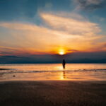 夕暮れの海辺に立つ人物のシルエットが、夏の終わりの静かな余韻を感じさせる情景｜懐かしい情景が静かによみがえる、やさしい記憶のイメージ写真