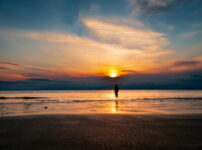夕暮れの海辺に立つ人物のシルエットが、夏の終わりの静かな余韻を感じさせる情景｜懐かしい情景が静かによみがえる、やさしい記憶のイメージ写真