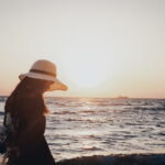 夕暮れの海辺で女性が花を手に静かに佇む情景｜懐かしい情景が静かによみがえる、やさしい記憶のイメージ写真